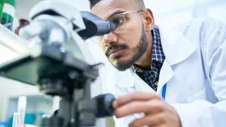 Man looking into a microscope to analyze the results of a clinical trial.