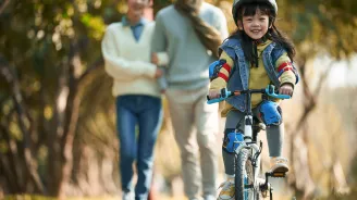 A little Girl Rides Her Bicycle While Her Parents Watch Happily From a Distance