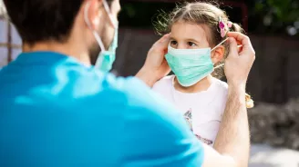 Father putting mask on daughter outdoors