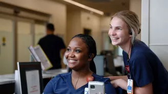 Two nurses from AdventHealth, smiling and looking to the left. 