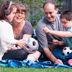 A family of four sitting on a blanket outside, playing with a soccer ball.