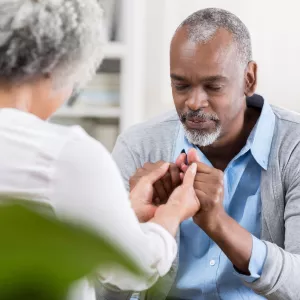 Elderly couple sitting across from each other, clasping hands, and praying together.