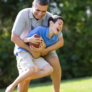 A father and son play football outdoors.