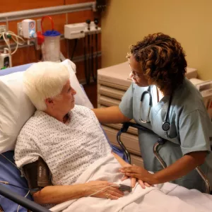 An older woman laying in a hospital bed talking to a nurse.