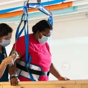 Physical therapist helping a patient in rehab with a walking exercise with the patient is being supported by a harness.