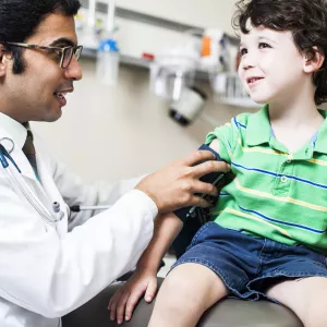 A child, sitting on an exam table, as a doctor takes his blood pressure.