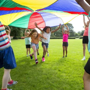 A group of children outside playing with a large multicolored parachute.