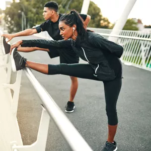 Two runners, stretching side by side, their legs extended and touching their toes.