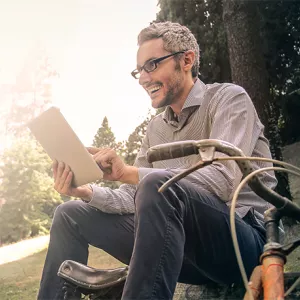 A man is sitting outside on the ground with a bicycle next to him.