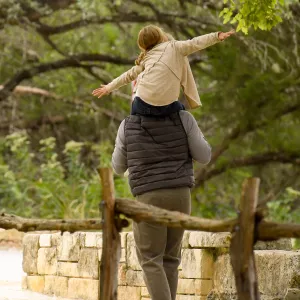 Father and daughter walking in the woods next to a fence.