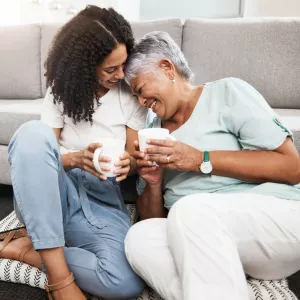 Relax, laughing and senior mother and daughter with coffee cup for home conversation, talking and bonding together