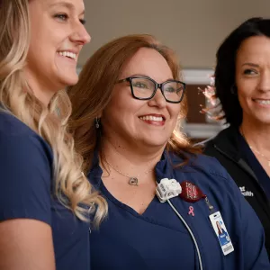 Three nurses stand together, smiling at something off the right side of the image.