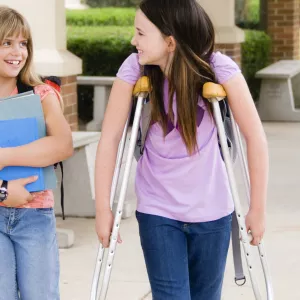 A girl on crutches walks with her friend at school