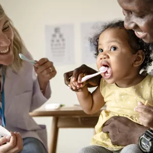 A dentist helps a father teach his daughter to brush her teeth