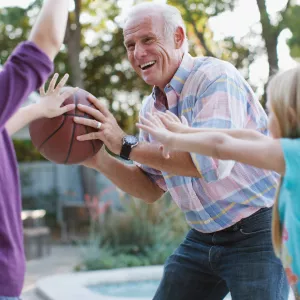 A grandfather plays basketball with his granddaughters. 