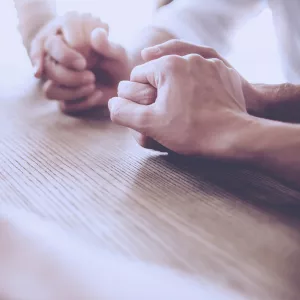 A group of friends holds hands in prayer.