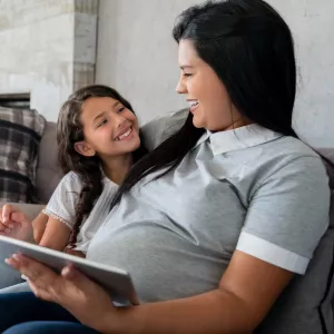 A pregnant mother and her daughter on the couch.