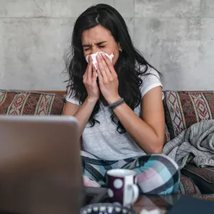 A woman sneezes into a tissue at home