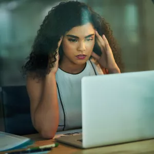 A woman massaging her temples at her desk at work.