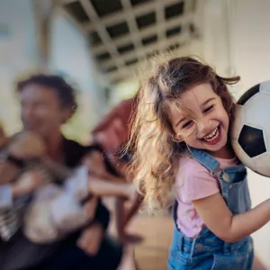 Young girl running with her family and carrying a soccer ball