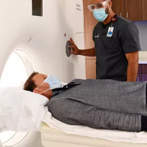 Man getting a CT scan while him and imaging tech wear masks.