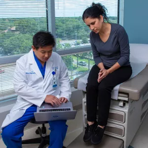 Iswanto Sucandy showing patient a something on a laptop while she's sitting on examination table.