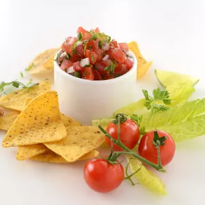 Dish of rustic tomato salsa surrounded by chips, garlic and tomatoes