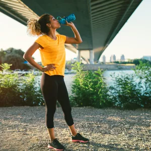 A woman drinking water on a trail, post run, during sunset.