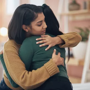 Two women hugging while at home.