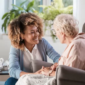 Woman smiling and holding hands with an elderly woman. 