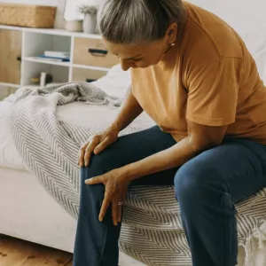 Woman sitting down at home and holding leg in pain.