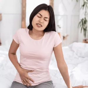 Woman sitting and holding lower abdomen in pain.