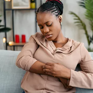 Woman sitting on a couch scratching her arm.