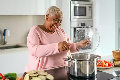 A Woman Gleefully Mixes a Large Pot on a Stove Top in a Modern Kitchen.