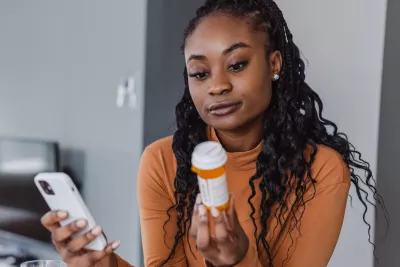 A Woman Examines a Pharmaceuticals Bottle While Holding Her Phone in the Other Hand