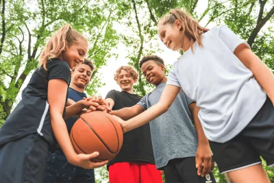 Five Teens Huddle Around a Basketball in a Park