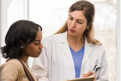 A young woman looks at a clipboard with her female doctor.