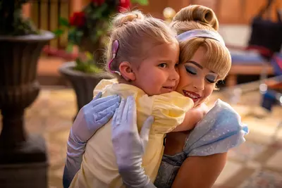 A little girl with a cochlear implant hugs Cinderella.