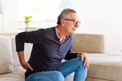 Older man holding his back with his hand while getting up off the couch.