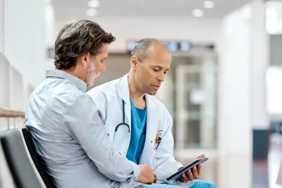 A physician and his male patient read documents together.