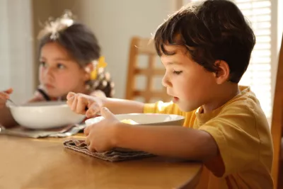 A young boy and girl eating together while at a dining room table together.