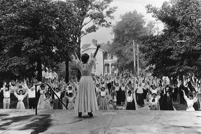 A woman leading out a group of people in breathing exercises while outdoors.
