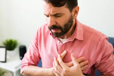 A main sitting and placing hands over chest in pain.