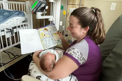 A mom reads to her baby in the AdventHealth for Children NICU in Orlando. Sitting in a rocking chair, she holds her baby while reading the book "Love You Forever."