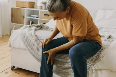 Woman sitting down at home and holding leg in pain.