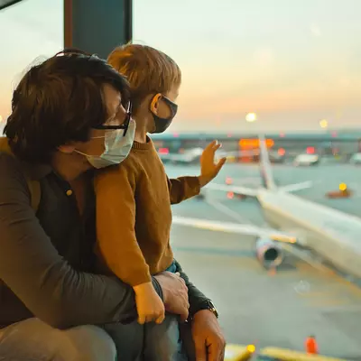 Father and son watch planes at the airport before boarding wearing face masks