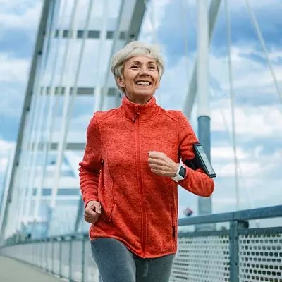 A Senior Woman Jogs Across a Bridge While Listening to Music