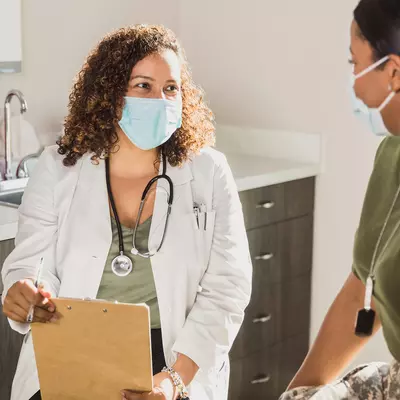 A Doctor Speaks to Her Patient in an Exam Room While Wearing a Face Mask.