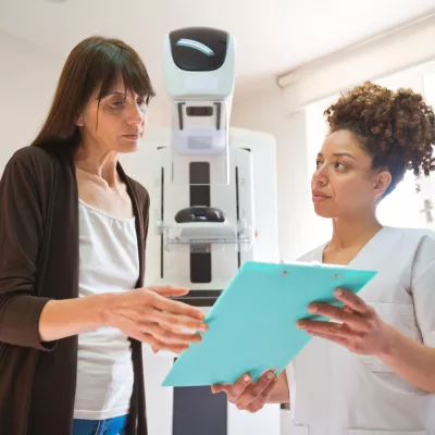 A Woman and a Provider Go Over a Chart in Front of Mammogram Machine