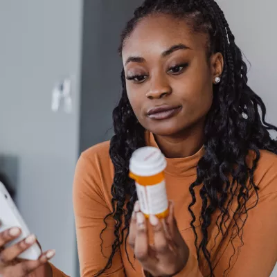 A Woman Examines a Pharmaceuticals Bottle While Holding Her Phone in the Other Hand